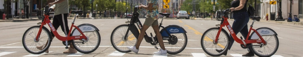The people walking their rental bikes across a crosswalk